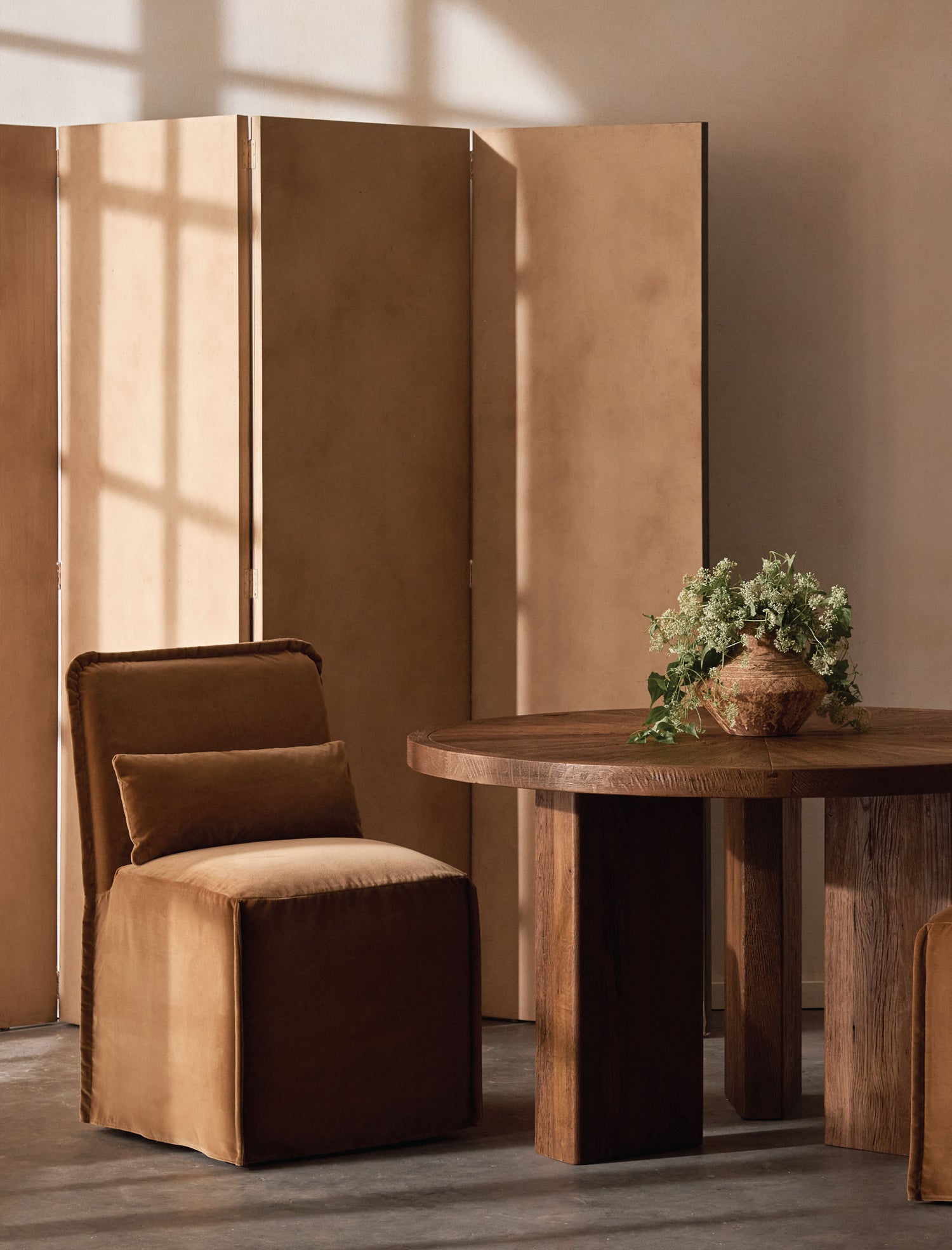 sixpenny melo armless dining chair table with a plant in a room with a beige wall and wooden floor.