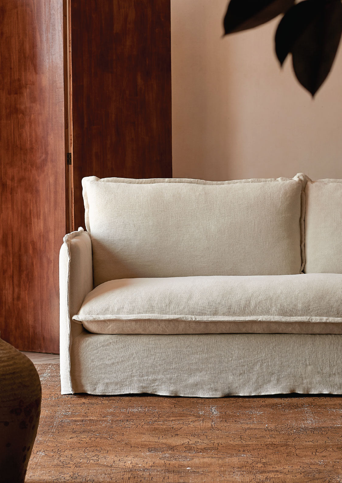 sixpenny Neva sofa against a wooden wall and beige wall with a plant leaf in the corner.