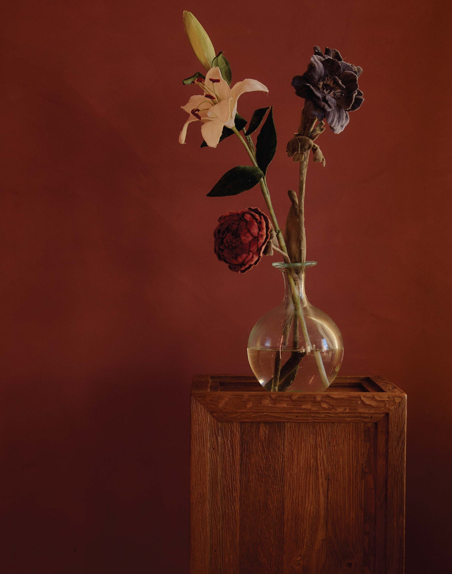 Glass vase with flowers on a sixpenny Rho pedestal against a red-brown background