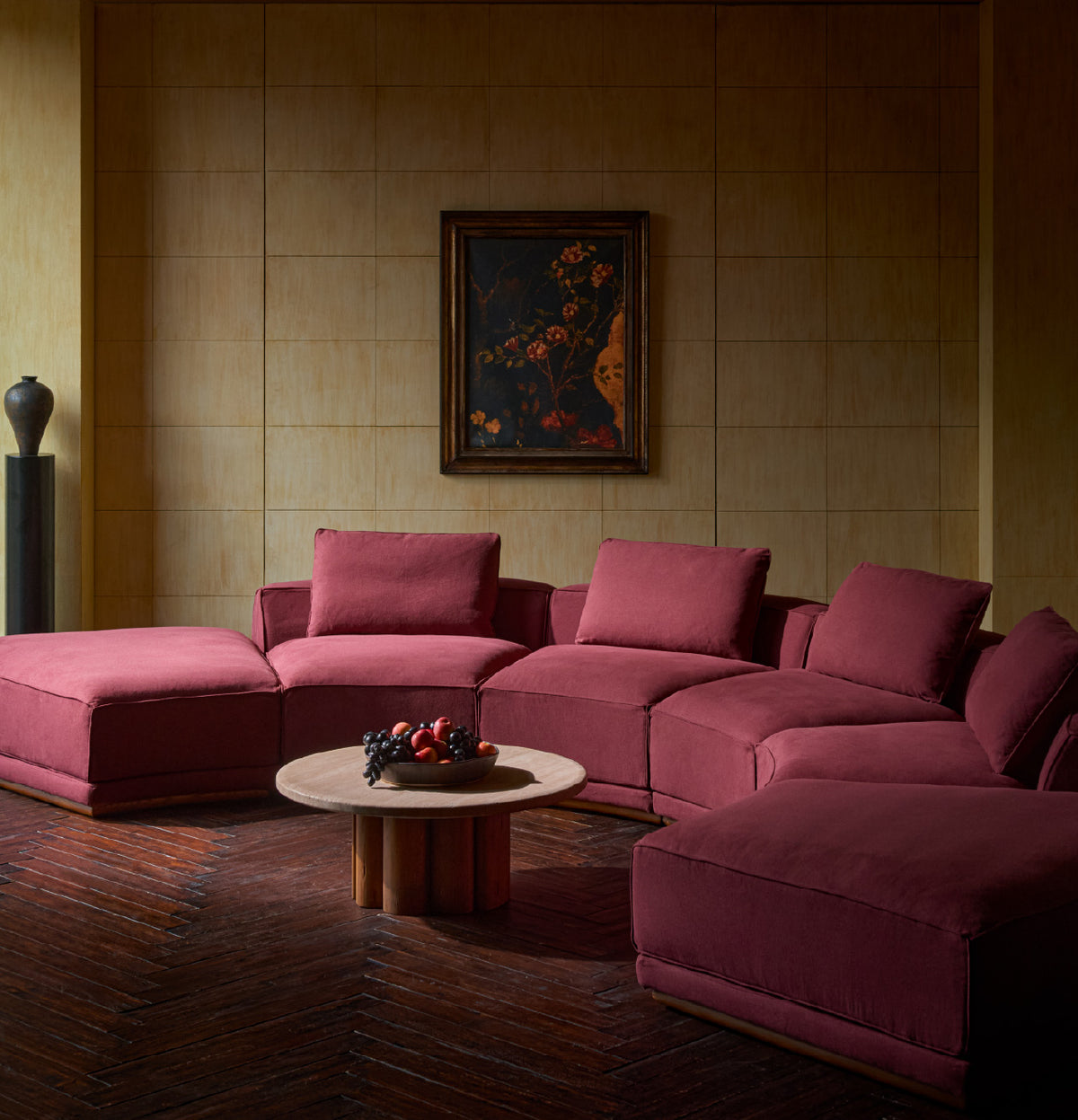 A sixpenny yogi half-moon sectional in summer plum, arranged in a dimly lit living room with an Enzo coffee table in Galata travertine and heritage pine. 