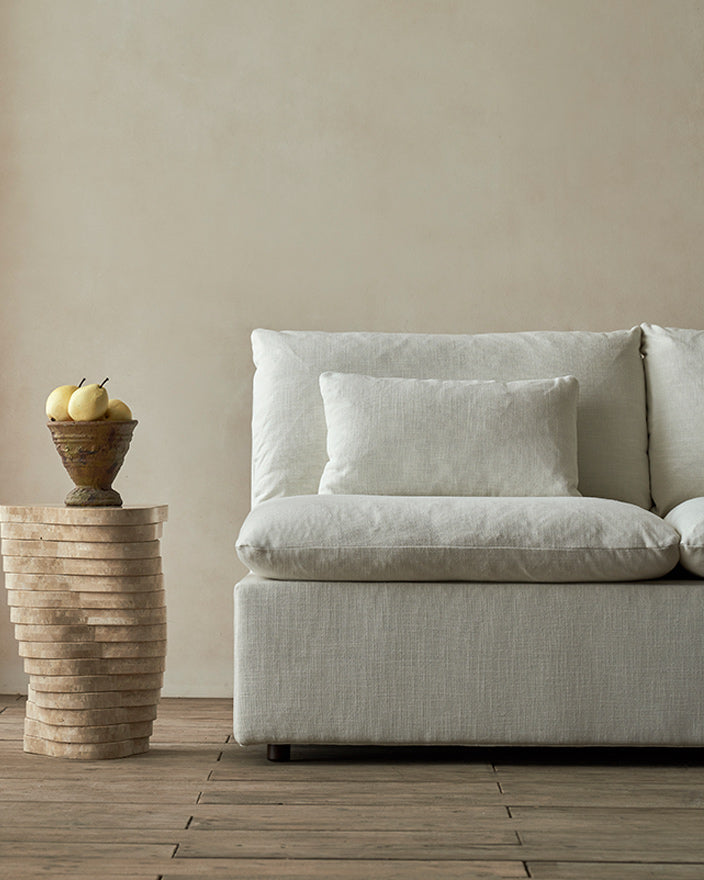 Aria Sleeper Sofa in Young Coconut, a powdery white Recycled Poly Linen, in a beige room with a sculpted stone side table decorated with a bowl of pears.