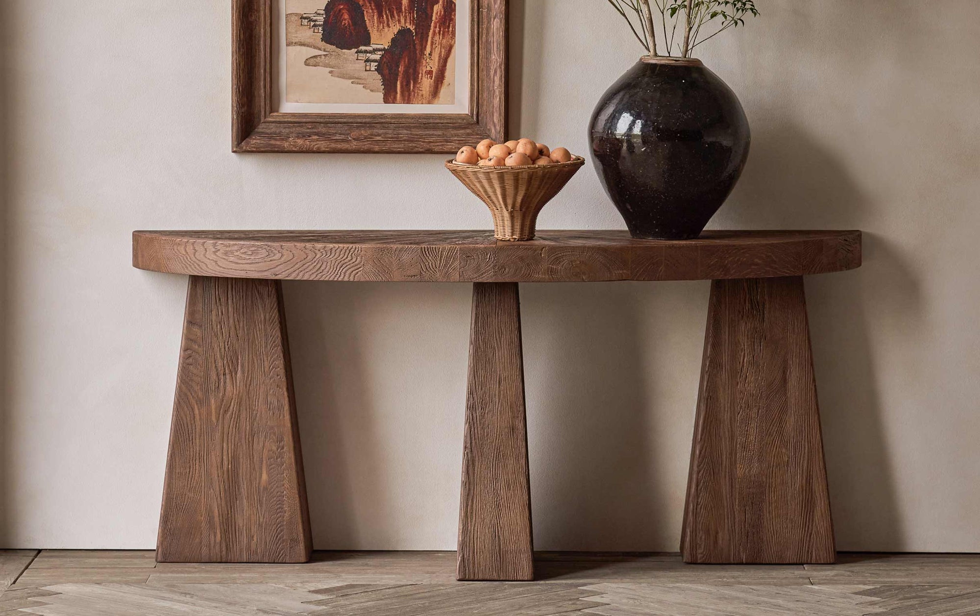 Tango Console Table in 100% Reclaimed Austrian Heritage Oak, a medium, bosc pear shade with earthy undertones, placed against a wall under a framed painting, decorated with a bowl of fruit and a large vase.