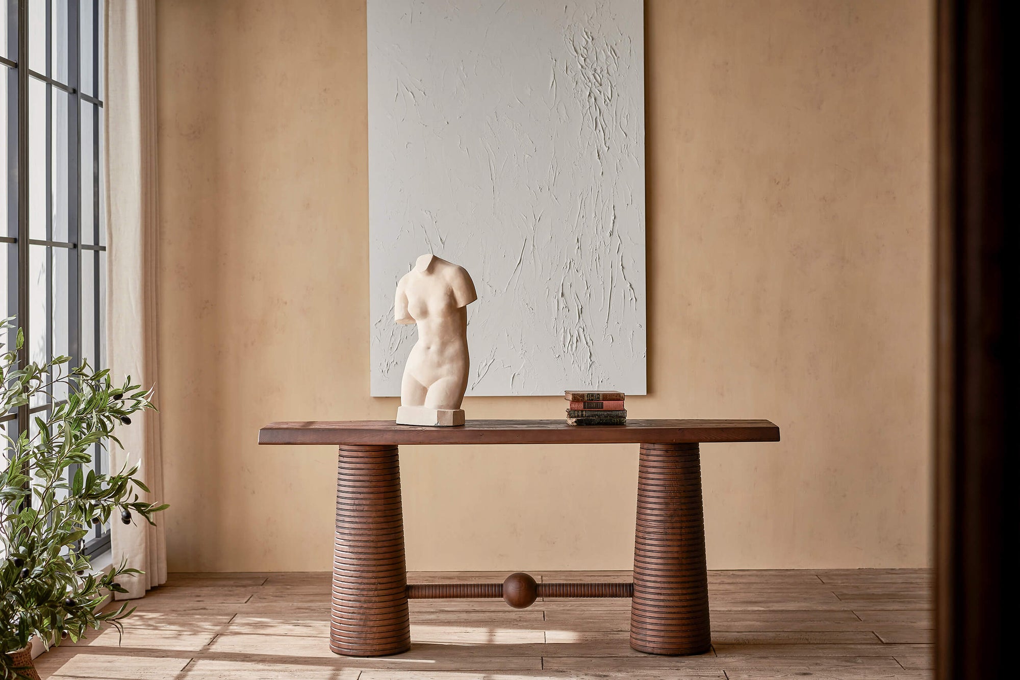 A statue and stack of books on top of the Zenia Console Table in Dusky Pine