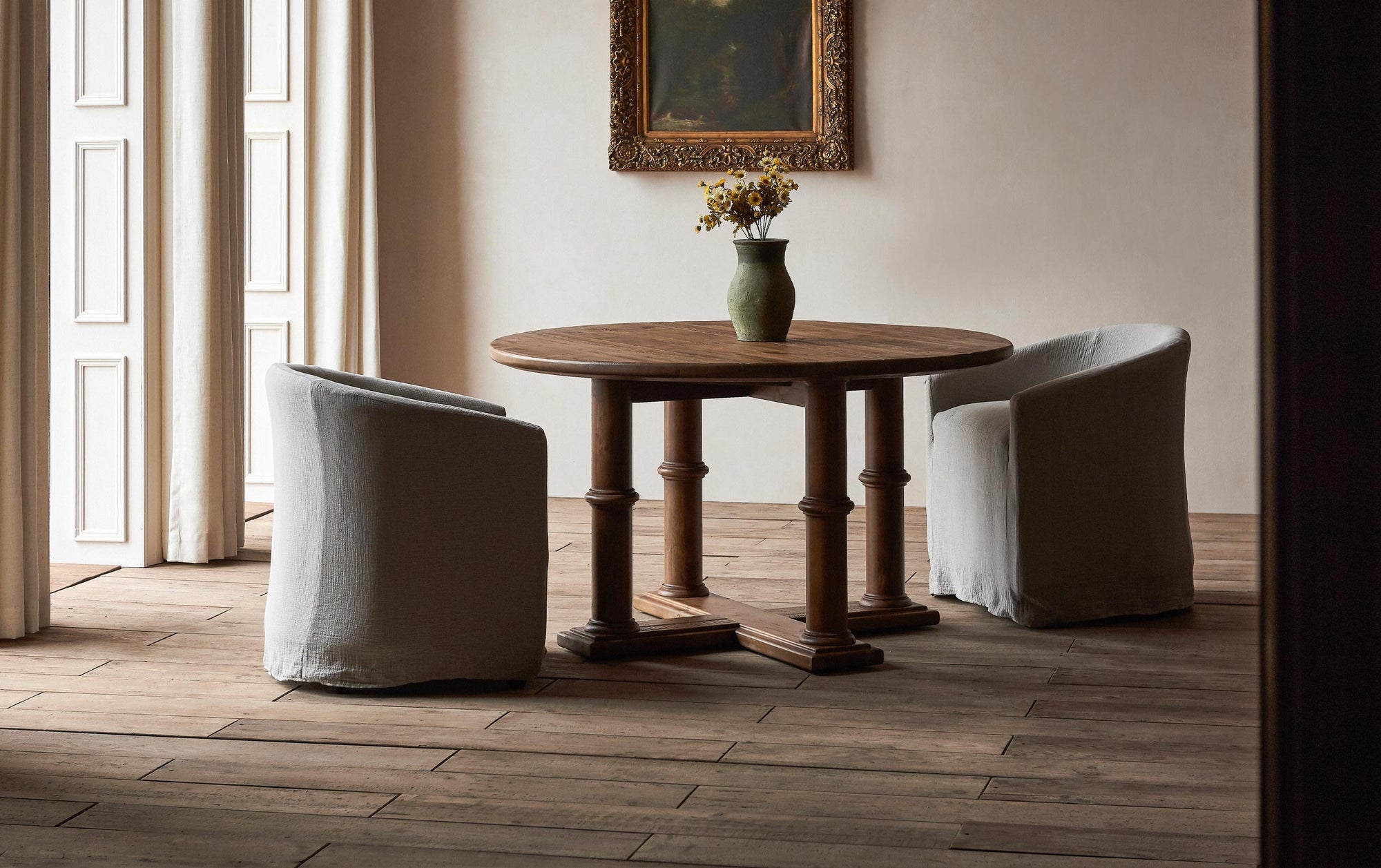 A set of Ziki Dining Chairs in Blanched Almond, a warm greige Washed Cotton Linen, placed around a Pia Dining Table with floral centerpiece in a naturally lit room.