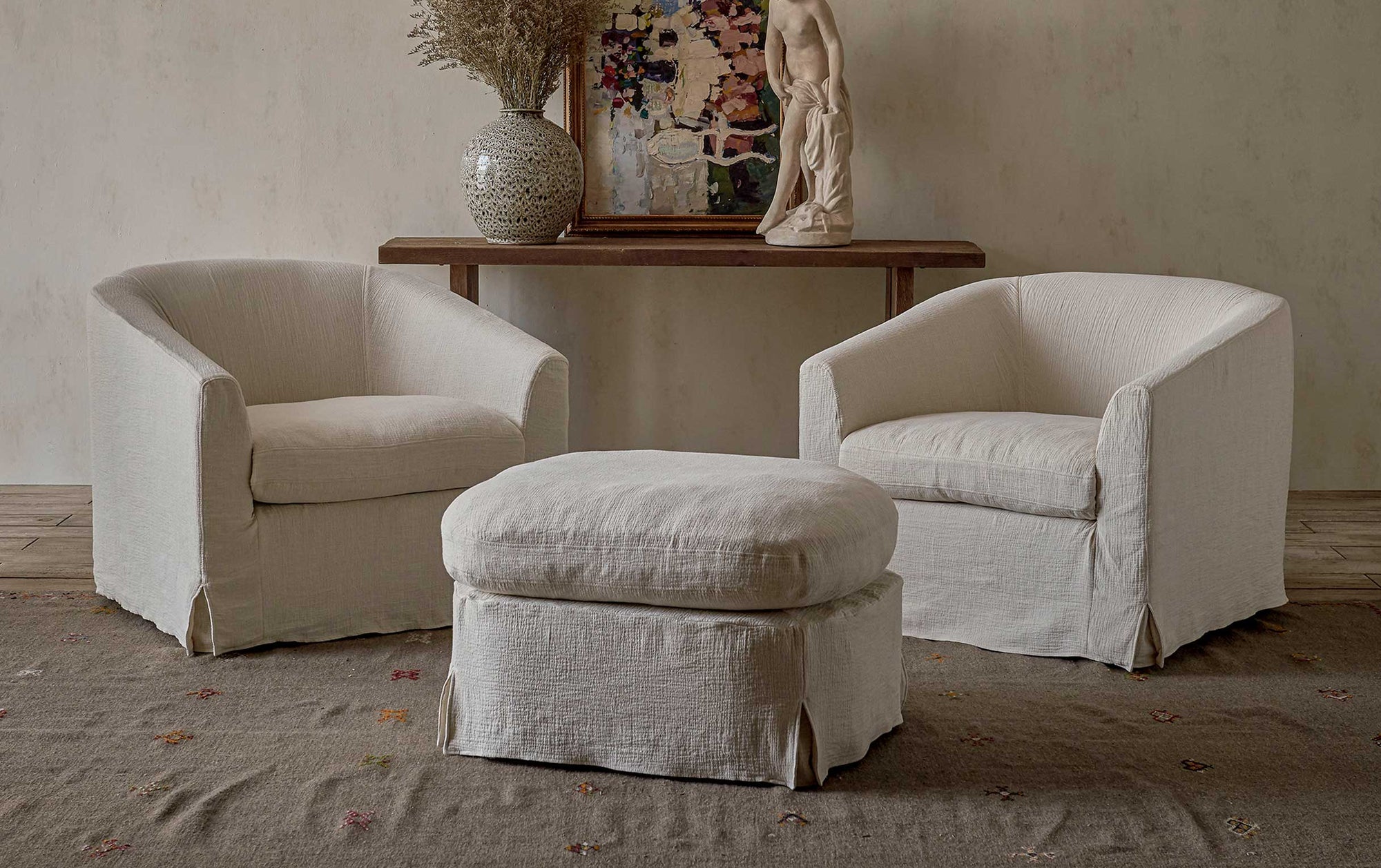 Ziki Chair Ottoman in Corn Silk, a light beige Washed Cotton Linen, placed in a room between two Ziki Chairs