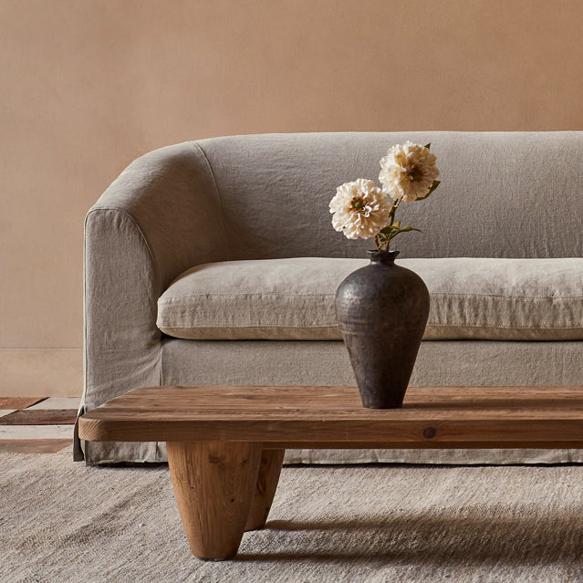 A Ziki Sofa in Oat Flour, a medium taupe Light Weight Linen, with flowers on top of a Theo Coffee Table
