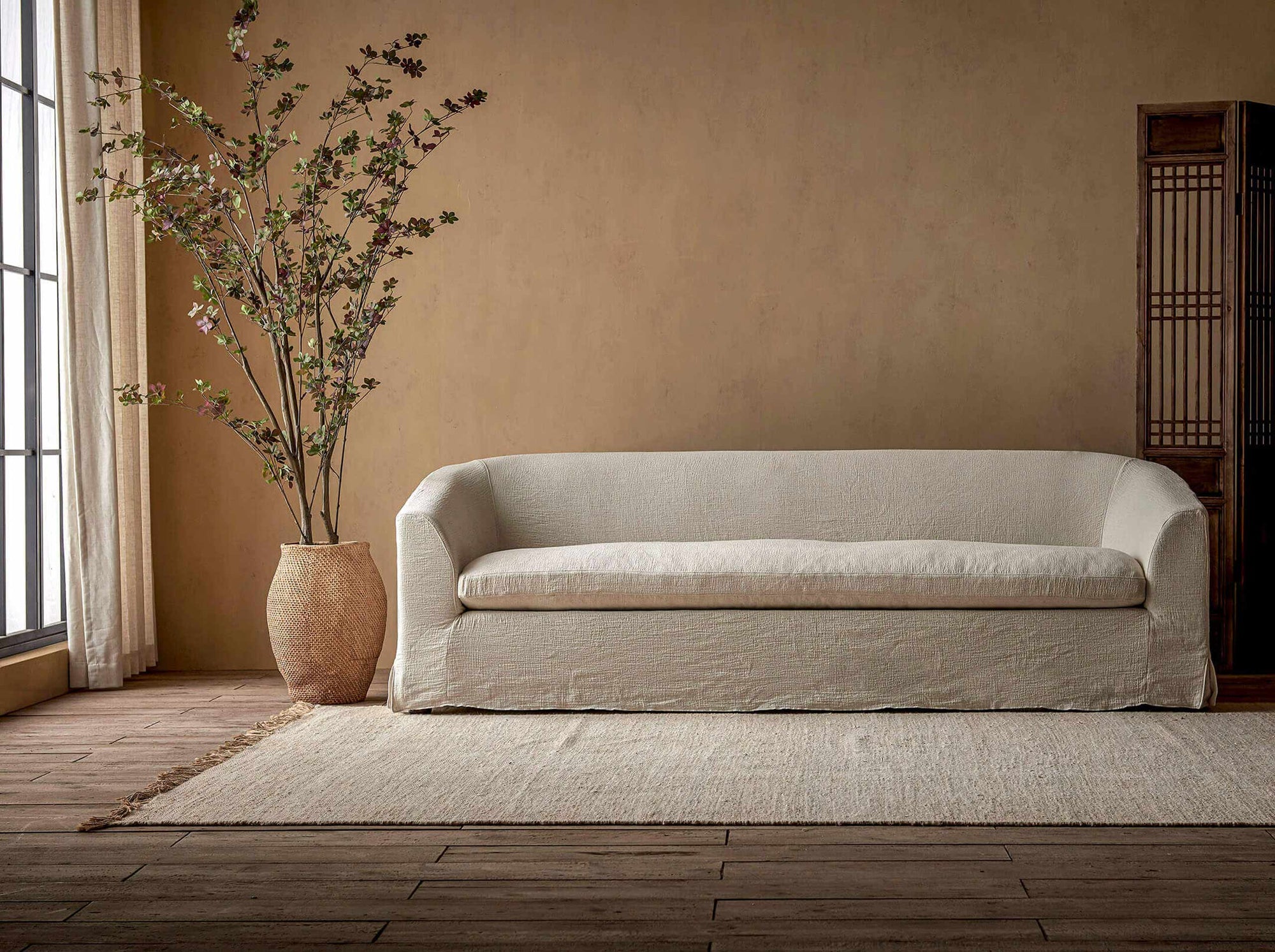Ziki 96" Sofa in Corn Silk, a light beige Washed Cotton Linen, placed in a room next to a potted tree