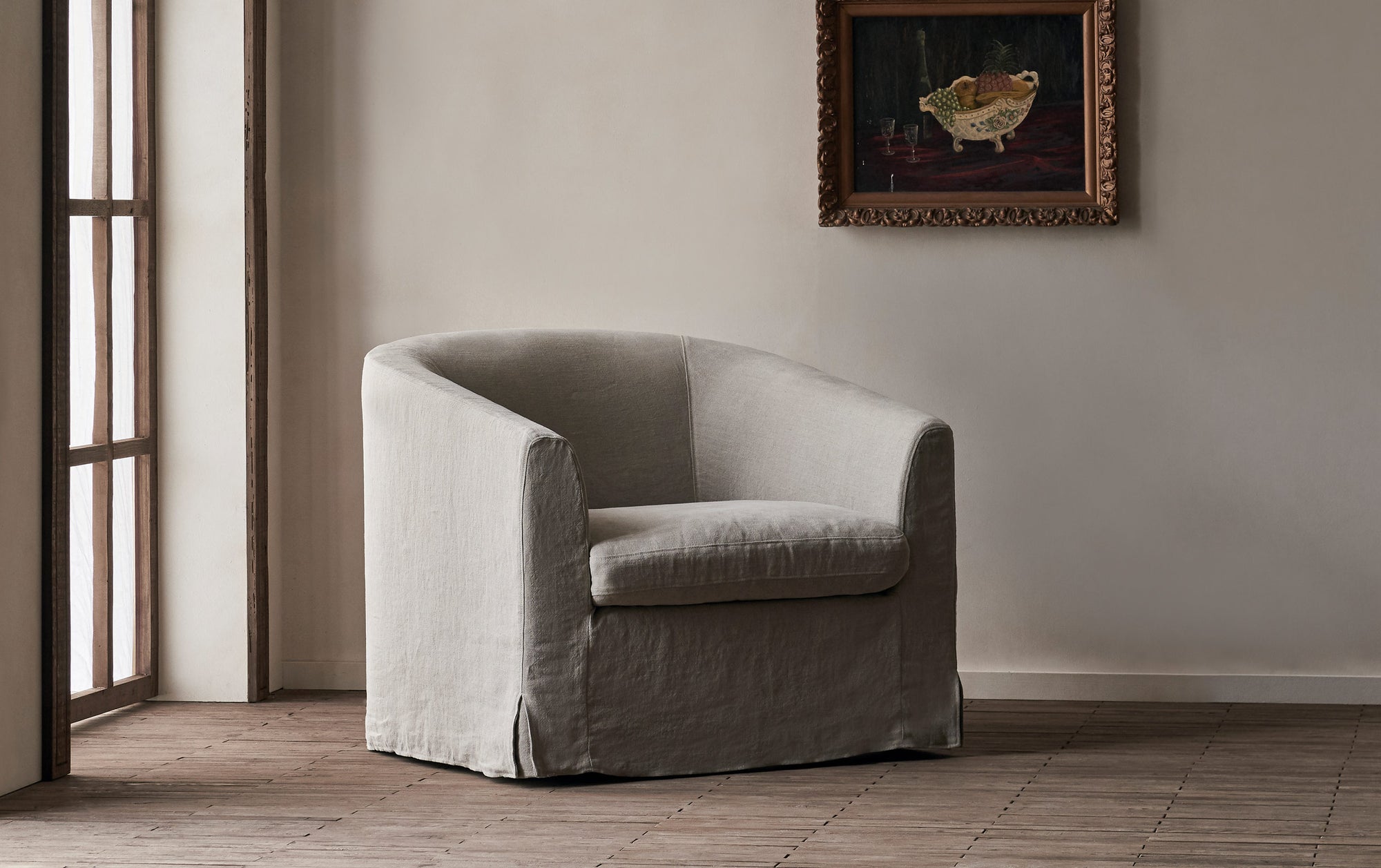 Ziki Swivel Chair in Oat Flour, a medium taupe Light Weight Linen, in front of a greige wall with a hanging framed painting