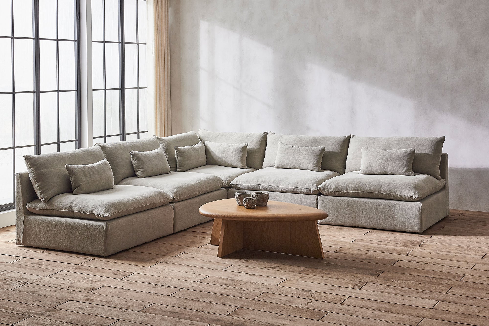 Aria Corner Sectional Sofa in Jasmine Rice, a light warm greige Medium Weight Linen, placed in a sunlit room with the Amina Coffee Table