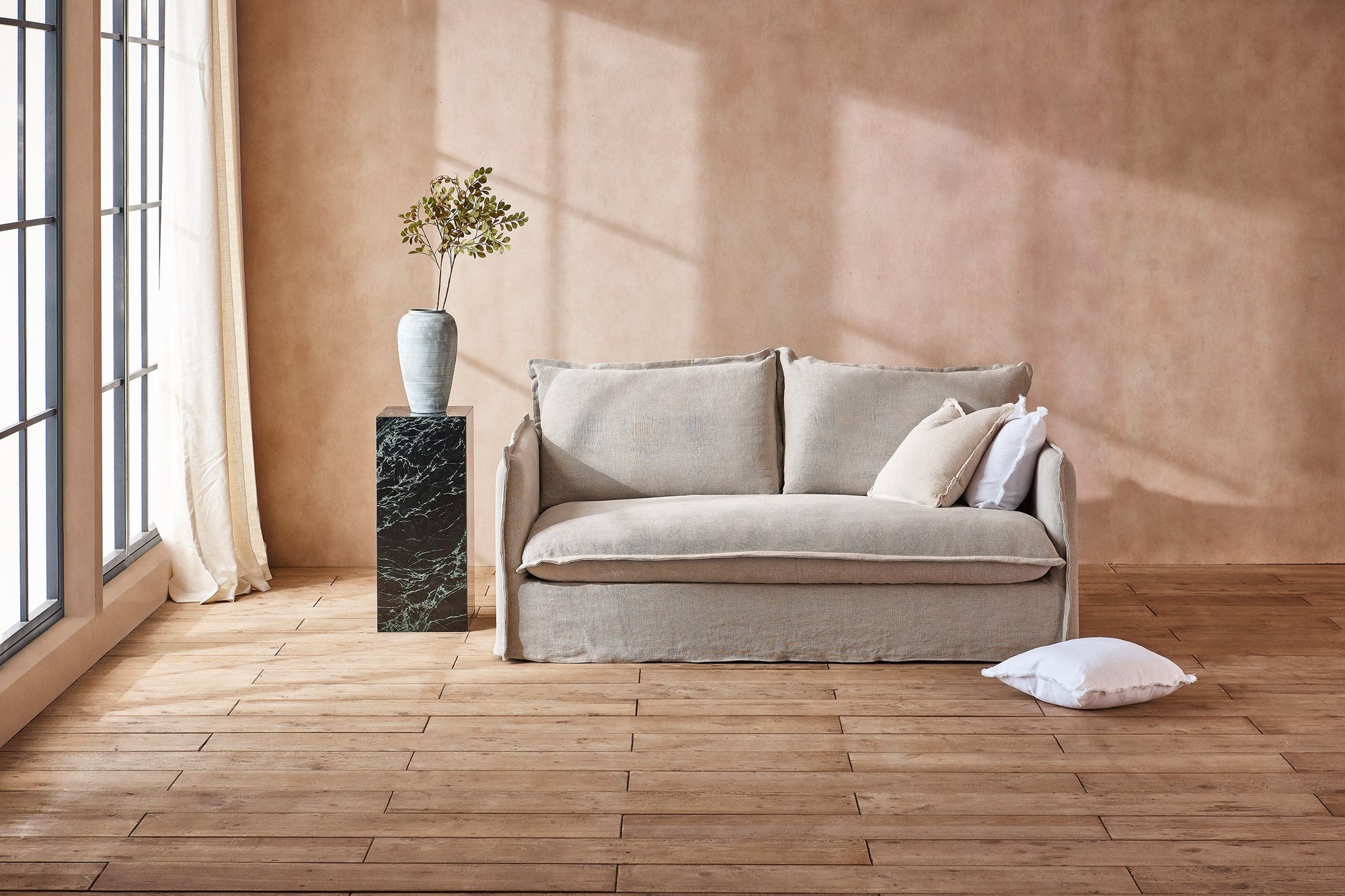Neva 72" Sofa in Jasmine Rice, a light warm greige Medium Weight Linen, placed in a sunlit room next to a plant in a vase on a decorative pillow