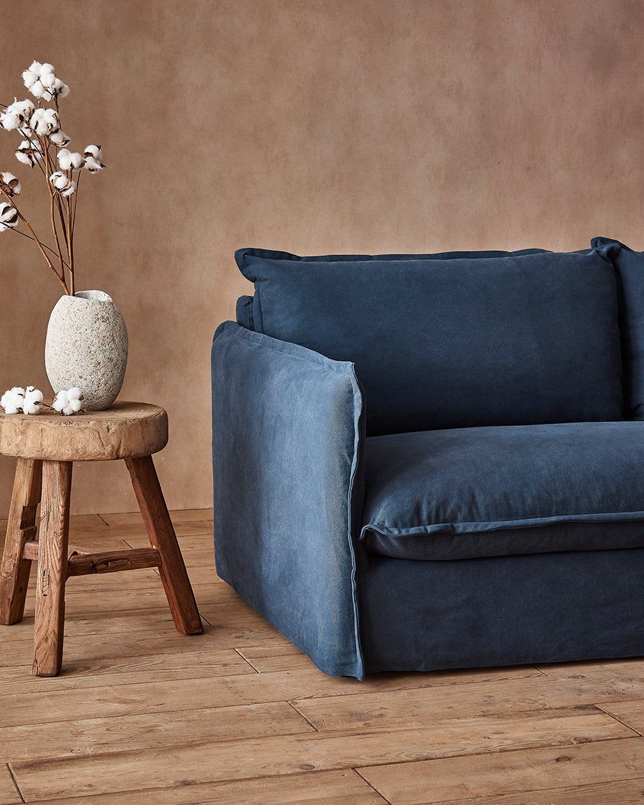 Neva Sofa in Ancient Indigo, a midnight blue Cotton Canvas, placed in a room next to a vase on a stool
