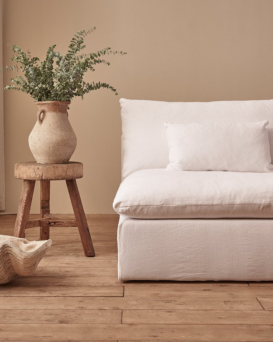 Aria Sofa in Pacific Pearl, a cool, pure white Cotton Linen, placed in a room next to a vase of ferns on a stool
