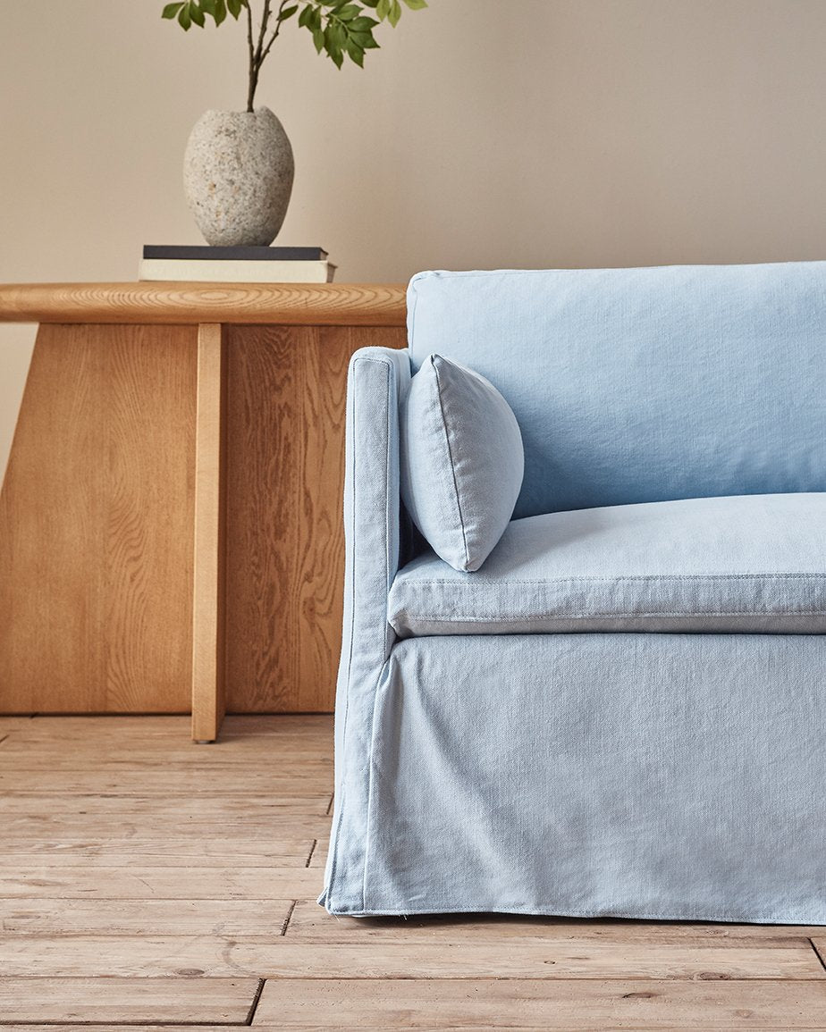 Gabriel Sofa in Salt Water, a light powder blue Cotton Linen,  placed in a room in front of a vase of plants on a table