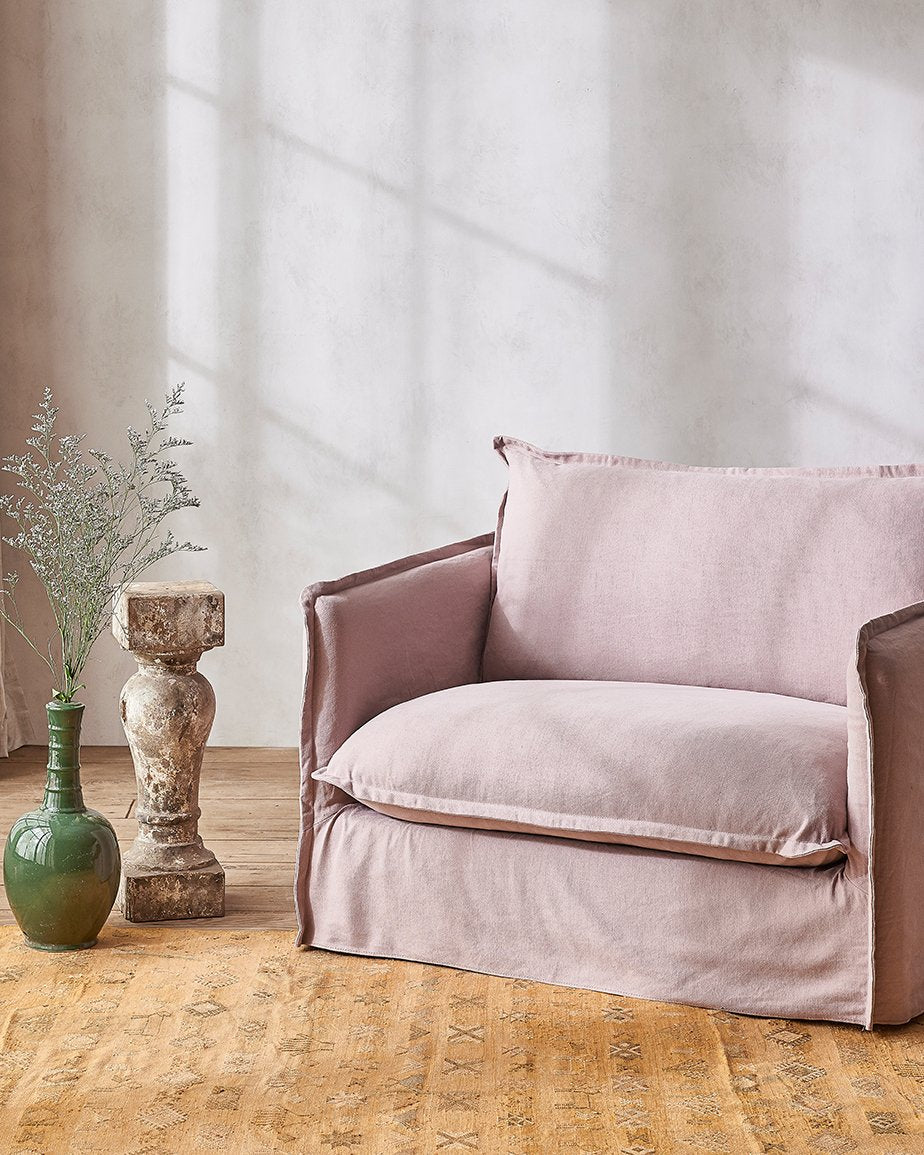 Neva Chair in Swatch of Sundazed Coral, a dusty mauve Cotton Linen, placed in a room next to a vase of flowering plants
