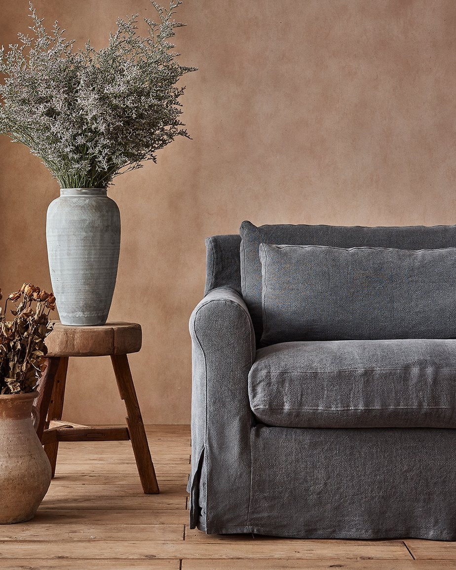 Elias Sofa in Black Pepper, a cool charcoal grey Light Weight Linen, placed in a room next to a stool and plants in vases