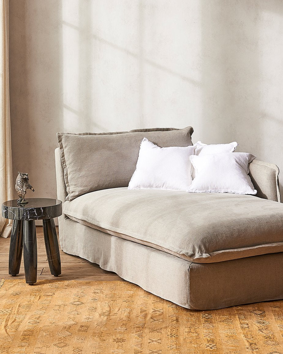 Neva Daybed in Cracked Pepper, a medium grey-beige Light Weight Linen, placed in a sunlit room next to a stool