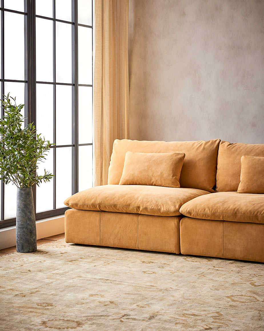 Aria Sectional Sofa in Mojave Glow, a tan Meridian Leather, placed in a sunlit room with a plant in a vase