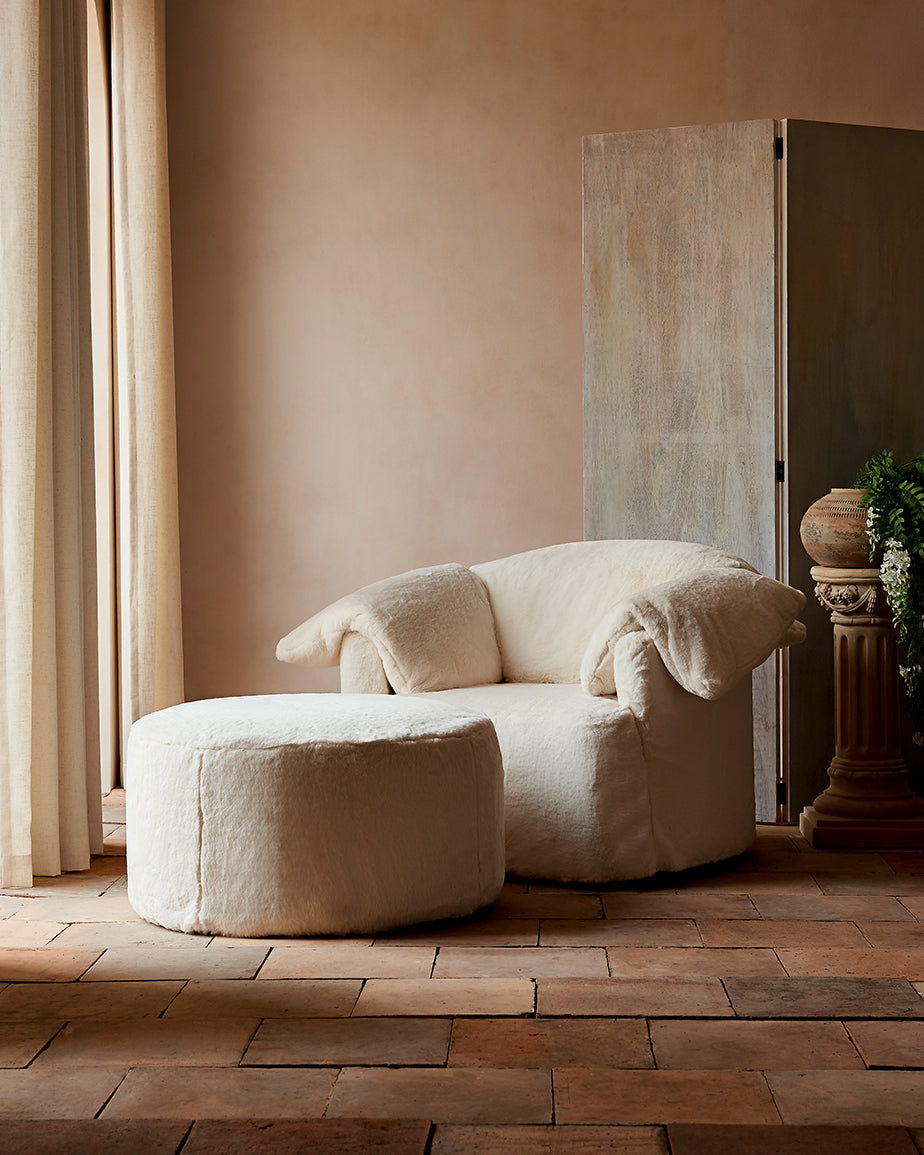 Loula Chair and Ottoman in Dandelion Poof, a creamy off-white Recycled Faux Fur, placed together in a sunlit room