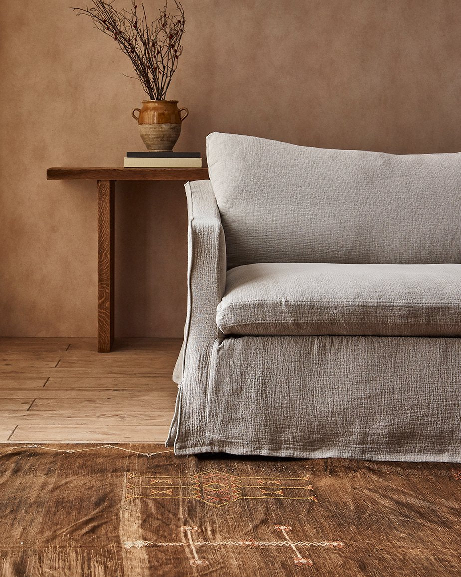 Gabriel Sofa in Blanched Almond, a warm greige Washed Cotton Linen, placed in a room in front of a vase of plants on a table